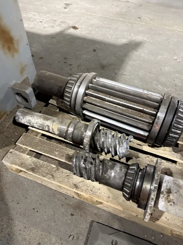 Ejes y piñones de acero retirados de un equipo, sobre un pallet en la planta