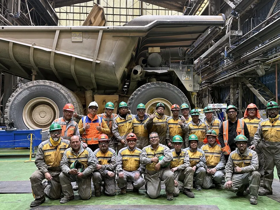 Equipo de terreno con casco y ropa de trabajo frente a un camión minero en un taller