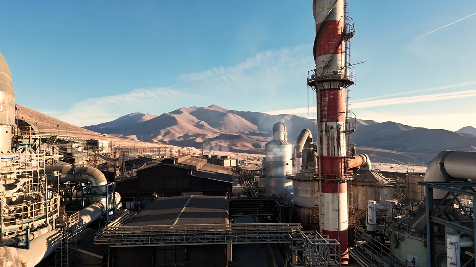 Planta de fundición con su chimenea y ductos, con la cordillera de fondo